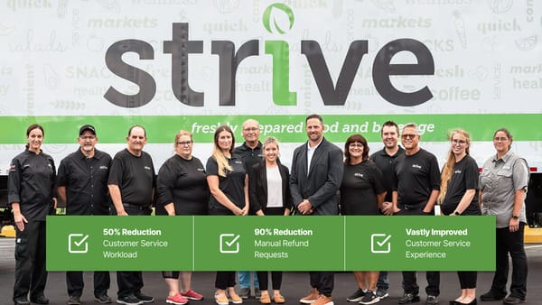 13 people stand in front of a large sign displaying the logo for Buffalo Strive.